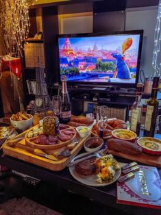 a table full of food and wine in front of a tv with the television on