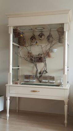 a white cabinet with glass shelves filled with birds and baskets on it's sides