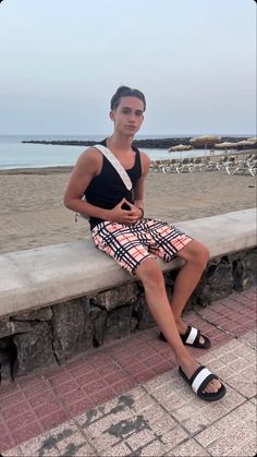 a man sitting on a stone wall next to the ocean with his legs crossed and wearing sandals