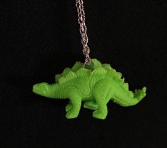 a green plastic dinosaur necklace on a black background with a chain hanging from it's neck