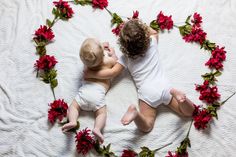 two babies in diapers laying on a bed with red flowers