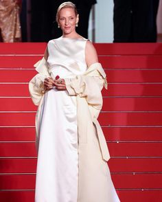 a woman in a white dress standing on a red carpet with her arms wrapped around her waist