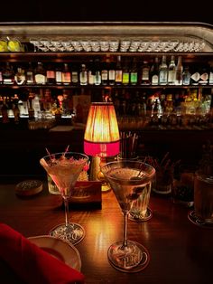 three martini glasses sitting on top of a wooden table in front of a bar filled with bottles