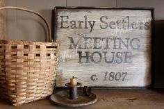 an old wooden sign next to a wicker basket and candle holder on a table