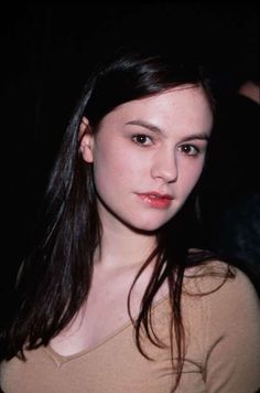 a young woman with long dark hair is posing for the camera, wearing a tan shirt