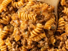 a wooden spoon filled with pasta and ground beef in a large skillet on top of a table