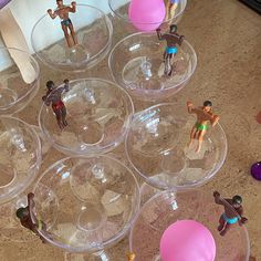 several plastic toy figurines sitting on top of clear bowls filled with water and sand