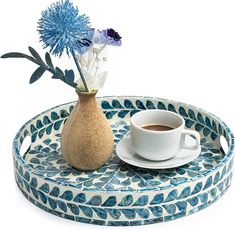 a blue and white tray with a cup of coffee on it next to a vase filled with flowers