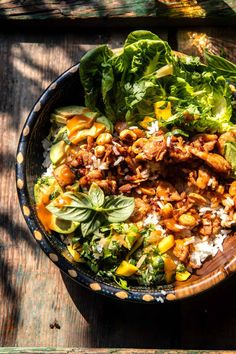 a bowl filled with lettuce, meat and other food on top of a wooden table