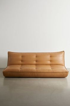 a brown leather couch sitting on top of a cement floor next to a white wall