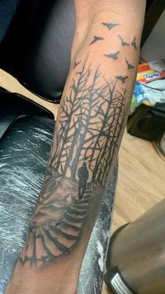 a man's arm with a tree and birds tattoo on it, in front of a chair