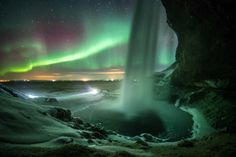 an aurora bore is seen in the night sky over a frozen lake and waterfall with green lights