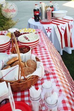 a picnic table set up with red and white gingham cloths, plates, cups, and food