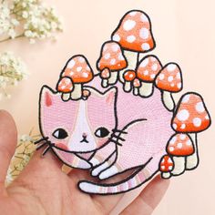 a hand holding a patch with a cat and mushrooms on it