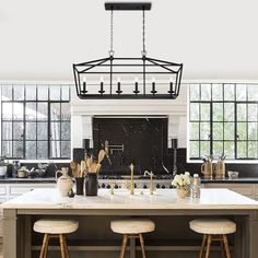 an island in the middle of a kitchen with three stools and a chandelier