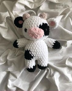 a crocheted stuffed cow laying on top of a white bed sheet with pink nose