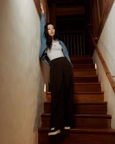 a woman standing at the bottom of stairs with her arms in the air and looking up