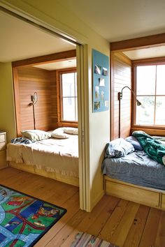 two beds in a room with wooden floors and windows on each side, one is made up