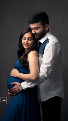 a man and woman pose for a photo in front of a dark background, holding each other's pregnant belly