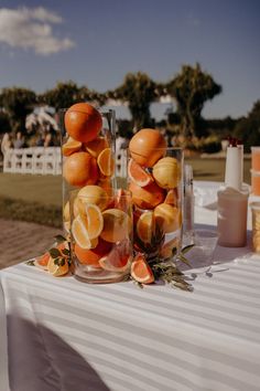 oranges are arranged in glass vases on a white table cloth at an outdoor event