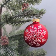 a red christmas ornament hanging from a pine tree's branch with snowflakes on it