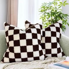 two brown and white pillows sitting on top of a couch next to a book near a window