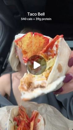 a woman is holding up a taco bell in her hand while sitting in the back seat of a car