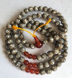 a close up of a beaded necklace on a white surface with an orange tassel