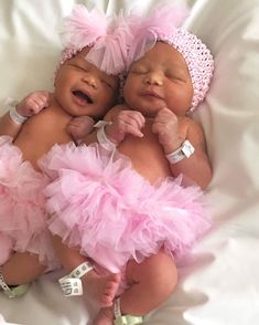 two baby babies laying next to each other on a white sheet covered bed with pink ruffles