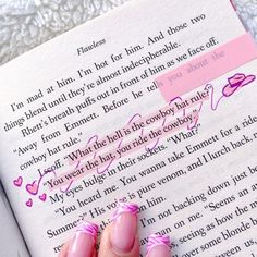 a person's hand with pink fingernails holding a book