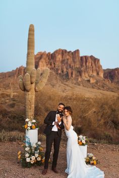 a newly married couple standing in front of a cactus