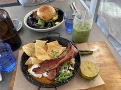 a plate with bacon, lettuce and tortilla chips next to a bottle of green juice