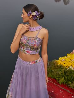 A three-piece lilac floral lehenga set from the Nikita Tiwari collection. This beautiful lilac floral pleated lehenga is paired with a printed bustier blouse. The lilac color with hand-embroidery work enhances the graceful georgette lehenga. The hand-embroidered blouse has intricate pearl-sequin details with floral print. The outfit is completed with a long floral jacket in viscos georgette material. Lavender Floral Embroidered Sets For Wedding, Fitted Purple Sharara With Floral Embroidery, Fitted Lavender Sharara For Reception, Fitted Lavender Floor-length Lehenga, Fitted Floor-length Lavender Lehenga, Fitted Lavender Choli For Reception, Fitted Lavender Floor-length Set, Lavender Floor-length Sets For Reception, Fitted Purple Sets With Floral Embroidery