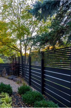 a black fence in the middle of a garden with lots of trees and bushes around it