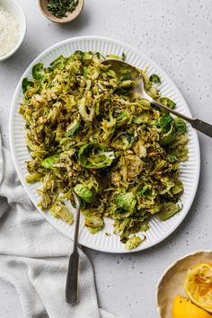 a white plate topped with shaved brussels sprouts next to bowls of rice and lemons