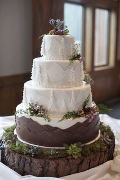 a three tiered white wedding cake with purple flowers and greenery on the top