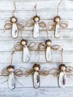 six ceramic angel ornaments hanging from twine on a white wooden background with twine