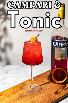 a red drink sitting on top of a wooden cutting board next to a bottle of campari and tonic