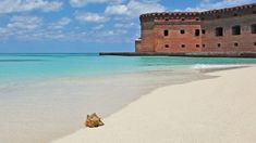 a large brick building sitting on top of a sandy beach next to the ocean with clear blue water