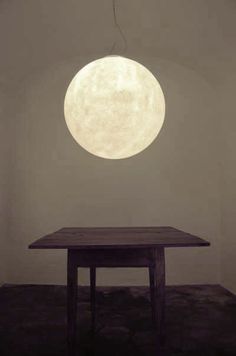 a table with a large moon hanging from it's ceiling in an empty room