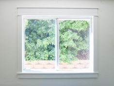 an empty room with a white window and green trees out the window in the background