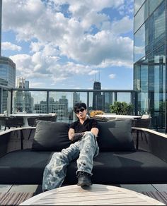 a man sitting on top of a black couch next to a wooden table and tall buildings