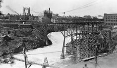 an old black and white photo of a bridge over a river with power lines above it