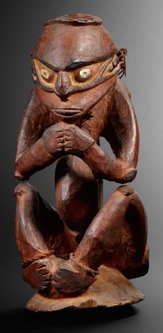 a wooden statue with eyes and hands on it's face, sitting on a piece of wood