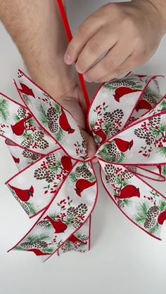 a person is holding a red and white christmas bow with pine cones on it,