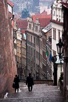 two people are walking up some stairs in an old city with tall buildings on either side