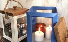 two lit candles sitting inside of a blue lantern on top of a wooden table next to other items