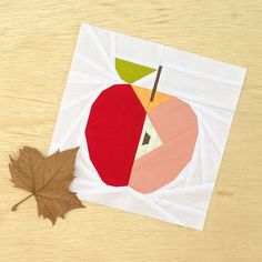 an apple cut in half on top of a wooden table next to a maple leaf