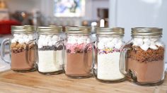 four mason jars filled with marshmallows and other treats on a counter top