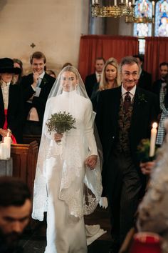 the bride and groom are walking down the aisle at their wedding ceremony, with candles in front of them